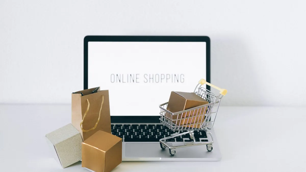 Laptop i mały wózek z paczką symbolizują sprzedaż i dobór produktów w e-commerce
