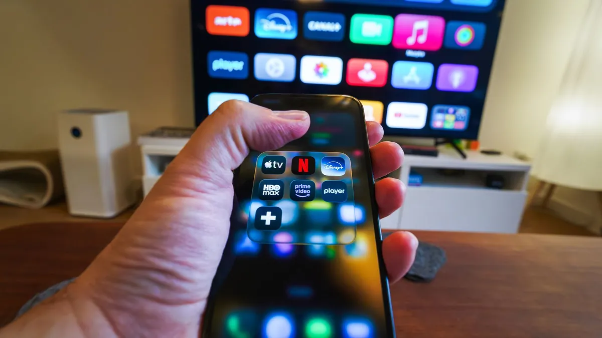 Dłoń ze smartfonem i ekran telewizora z aplikacjami symbolizują katalog treści oraz reklamę streamingową