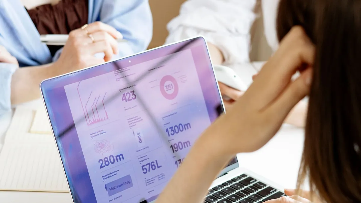 Kobiety planują kampanię przy laptopie i wykresach, analizując zasięg wielu formatów reklamowych