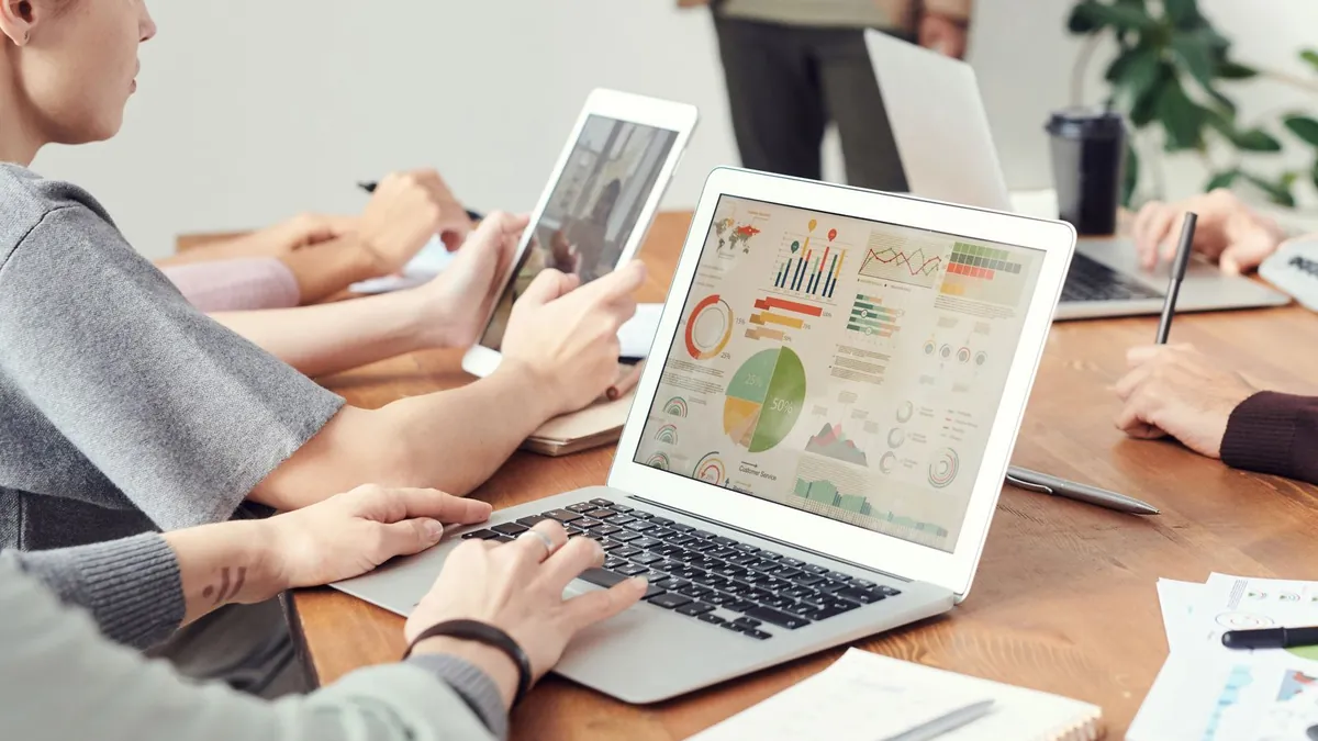 Zespół analizuje wykresy na laptopach, co symbolizuje kontrolę kosztu kliknięcia i porządkowanie kampanii Demand Gen