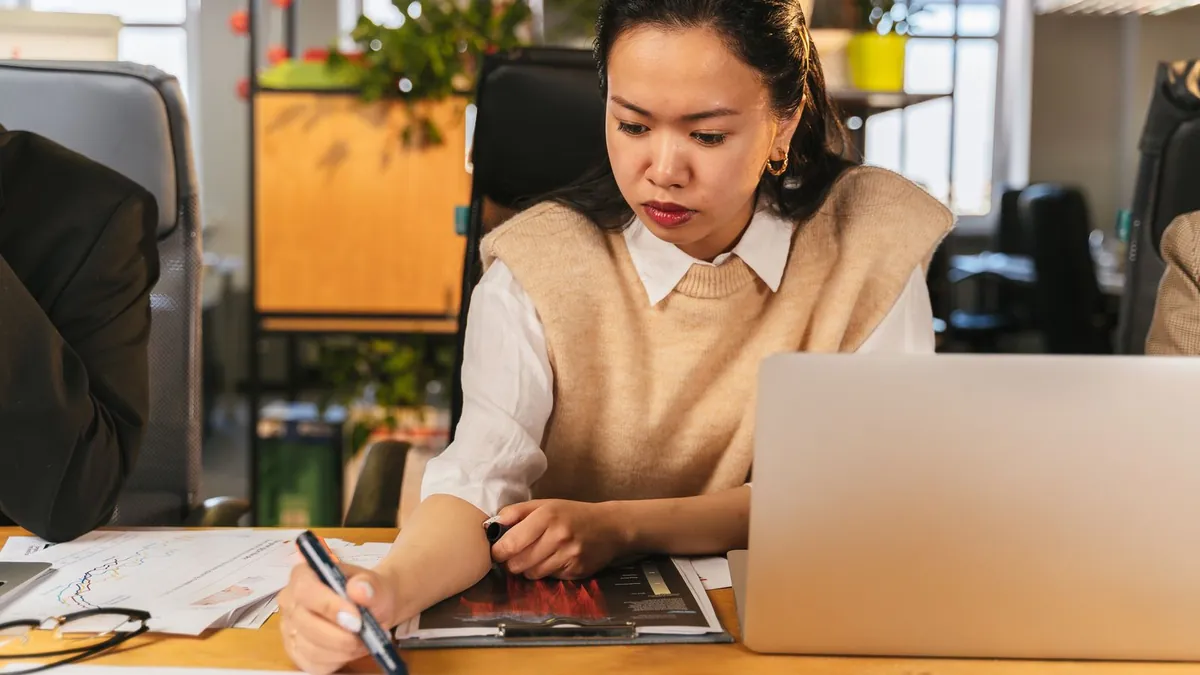 Kobieta przy biurku analizuje wykresy obok otwartego laptopa