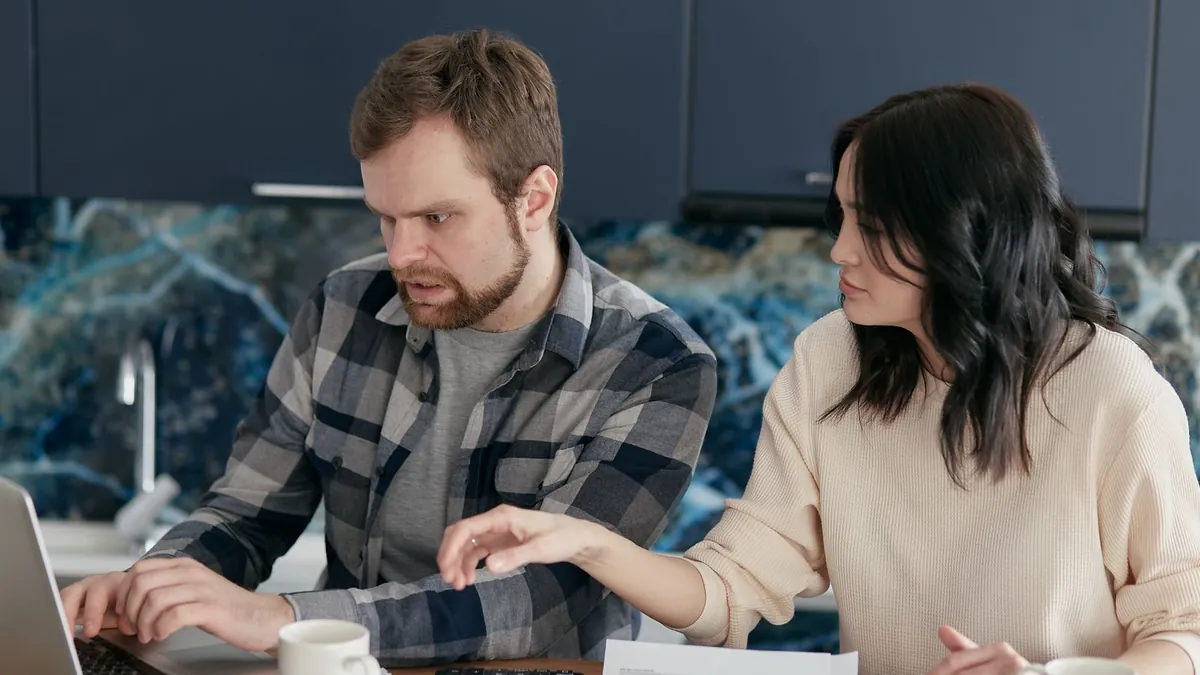 Dwie osoby analizują dokumenty i ekran laptopa przy stole